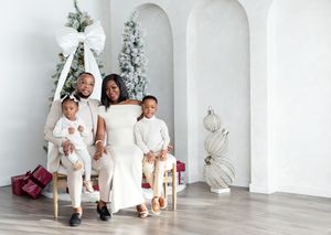 Family wearing coordinated white outfits poses in front of elegant white arches and holiday decor.
