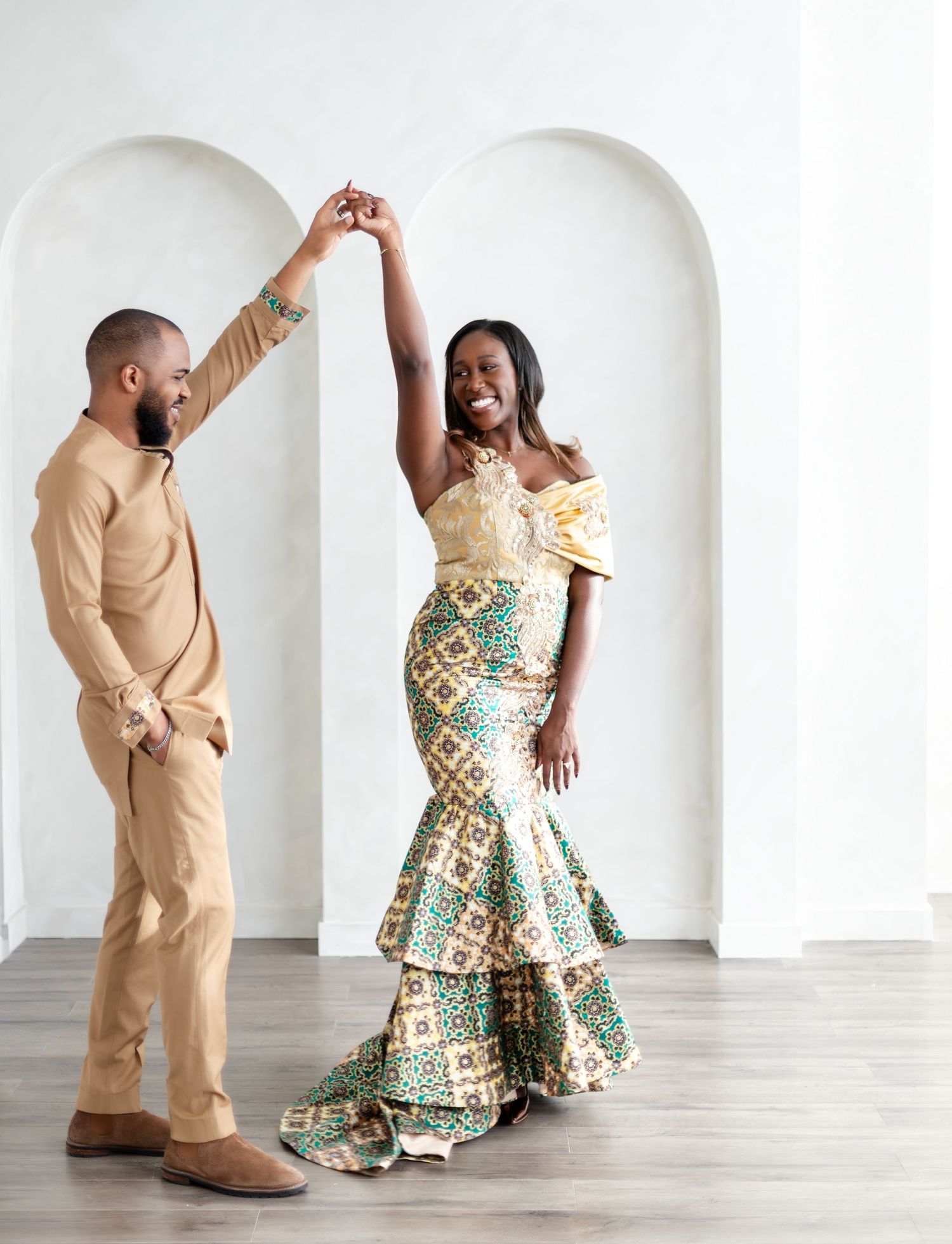 A couple dancing together in a studio, with the woman wearing a patterned dress and man in tan attire.