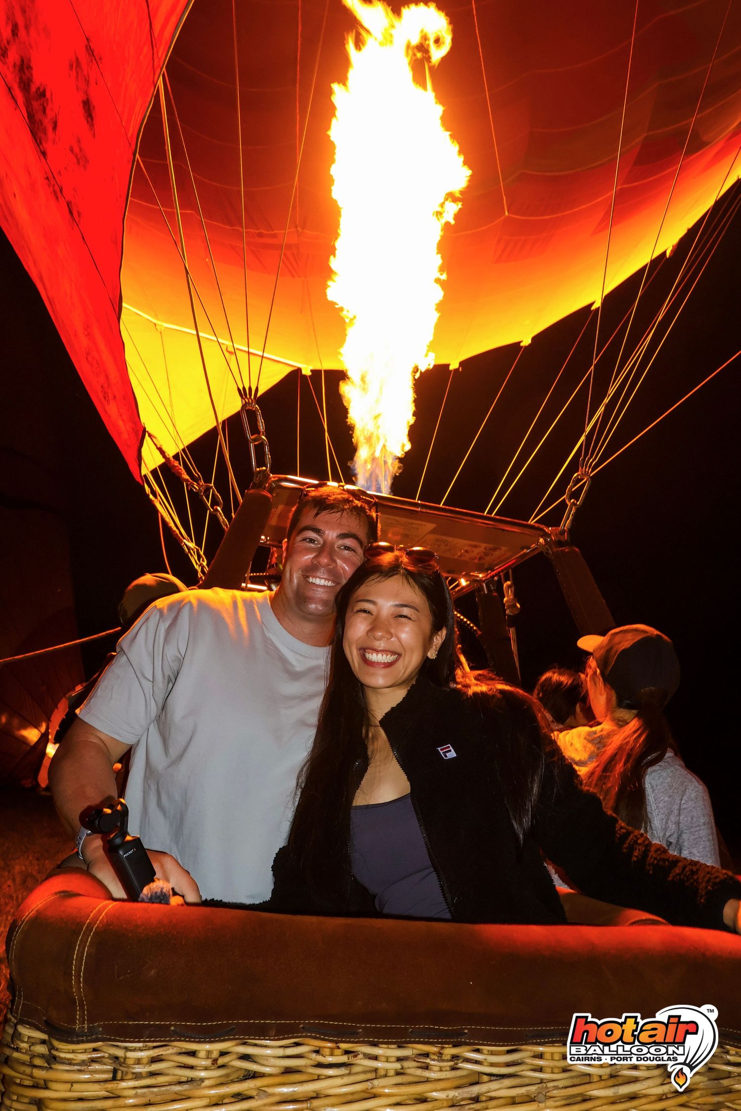 Couple smiling in front of a hot air balloon burner flame at night, captured by Hot Air Ballon Cairns. Cairns, Mareeba, Atherton, Australia