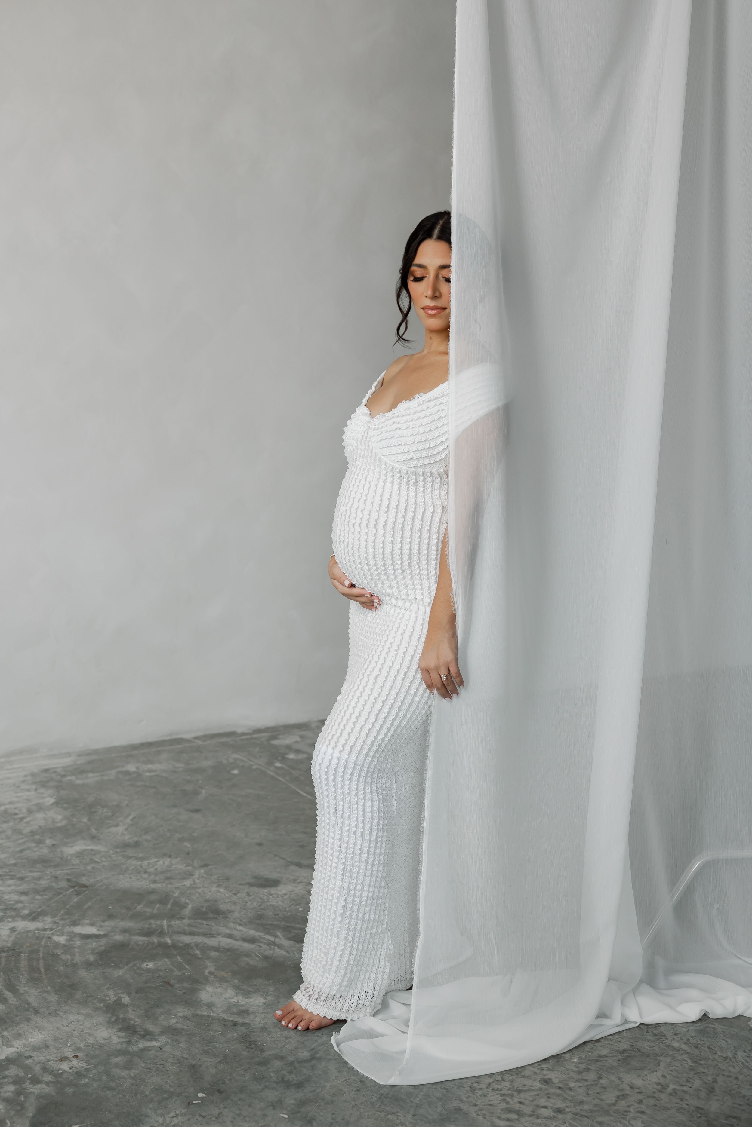 A pregnant woman standing alone in a studio.