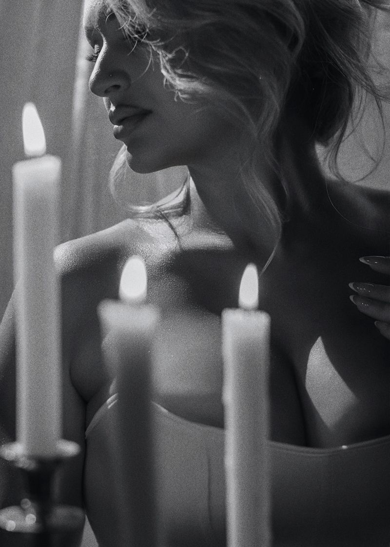 Black and white photo of a woman posing elegantly beside lit candles in soft candlelight.