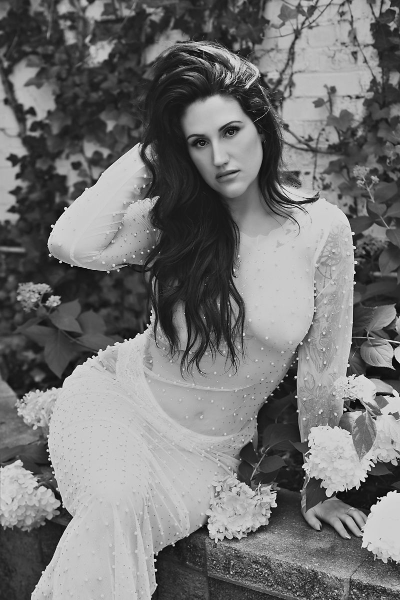 Black and white portrait of woman in lace dress against ivy wall background in romantic style.