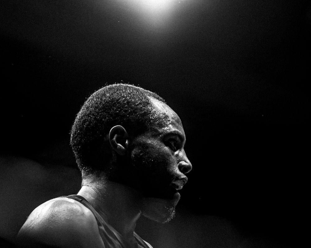 Black and white profile portrait of a male athlete under dramatic spotlight lighting.