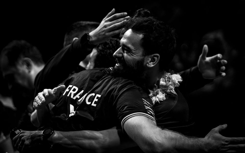 Black and white photo of French athletes embracing in celebration during a competitive sports event.
