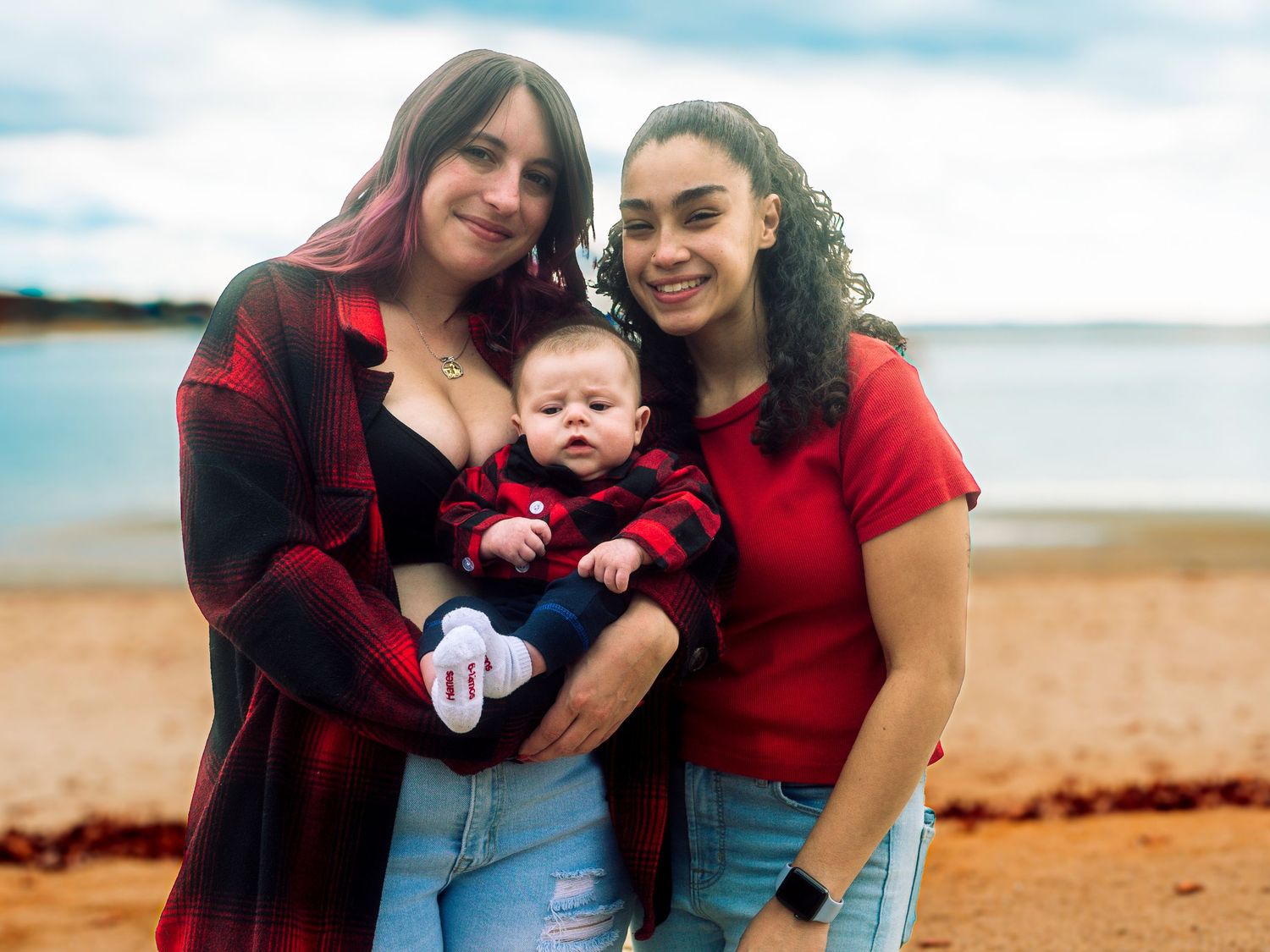 Family wearing red shirts poses together at beach during sunset for holiday photos.