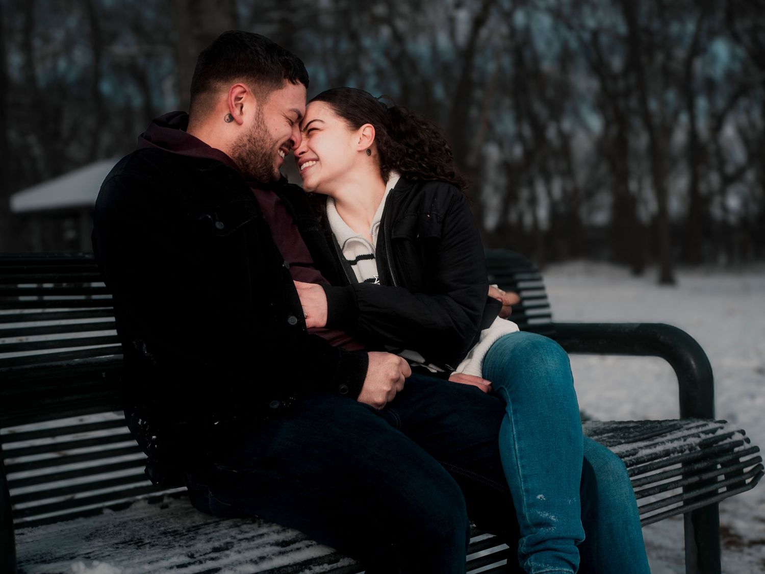 A couple shares an intimate moment while sitting together on a park bench in the snow.