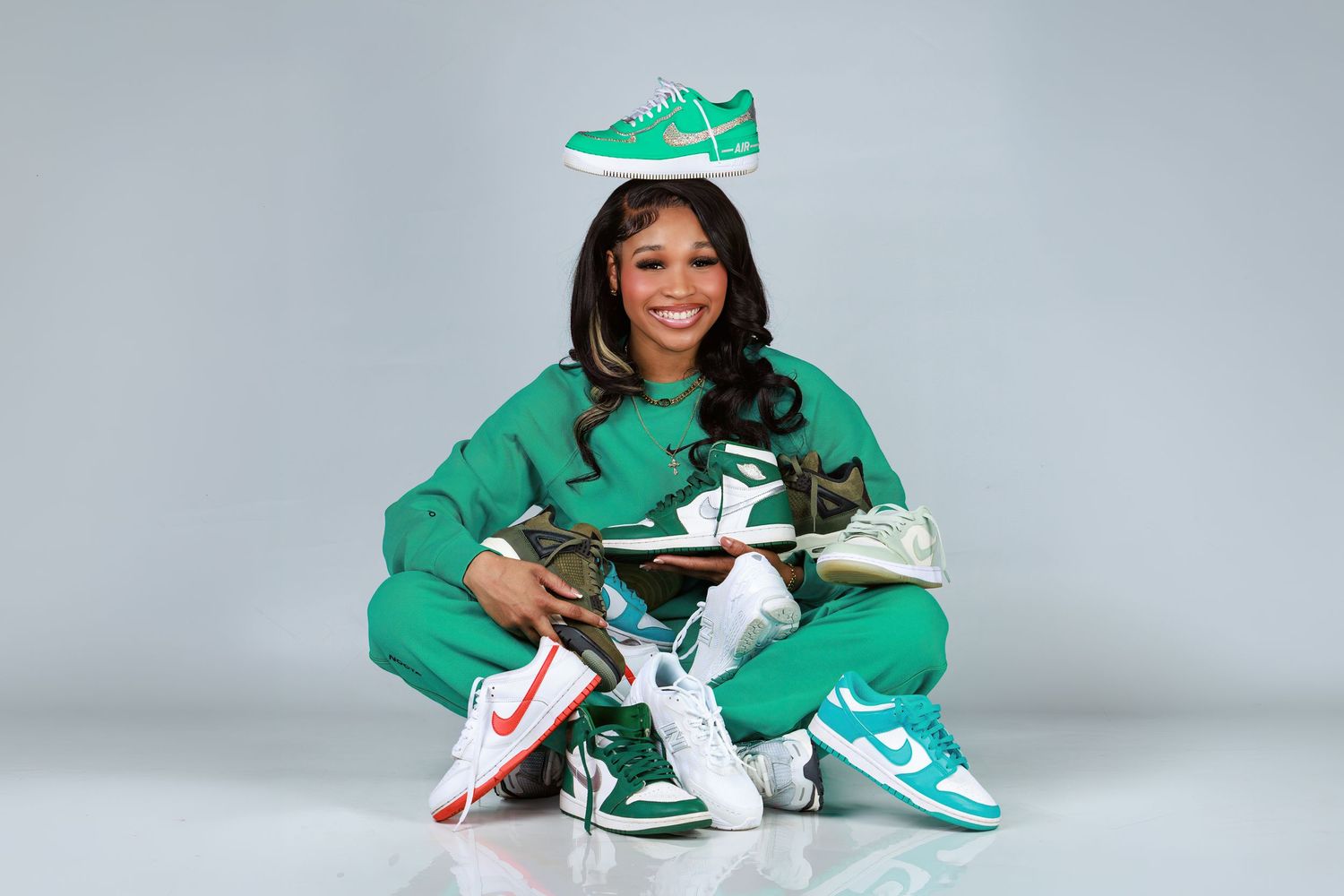Athletic figure in green tracksuit and matching sneakers poses with signed merchandise against gray studio backdrop.