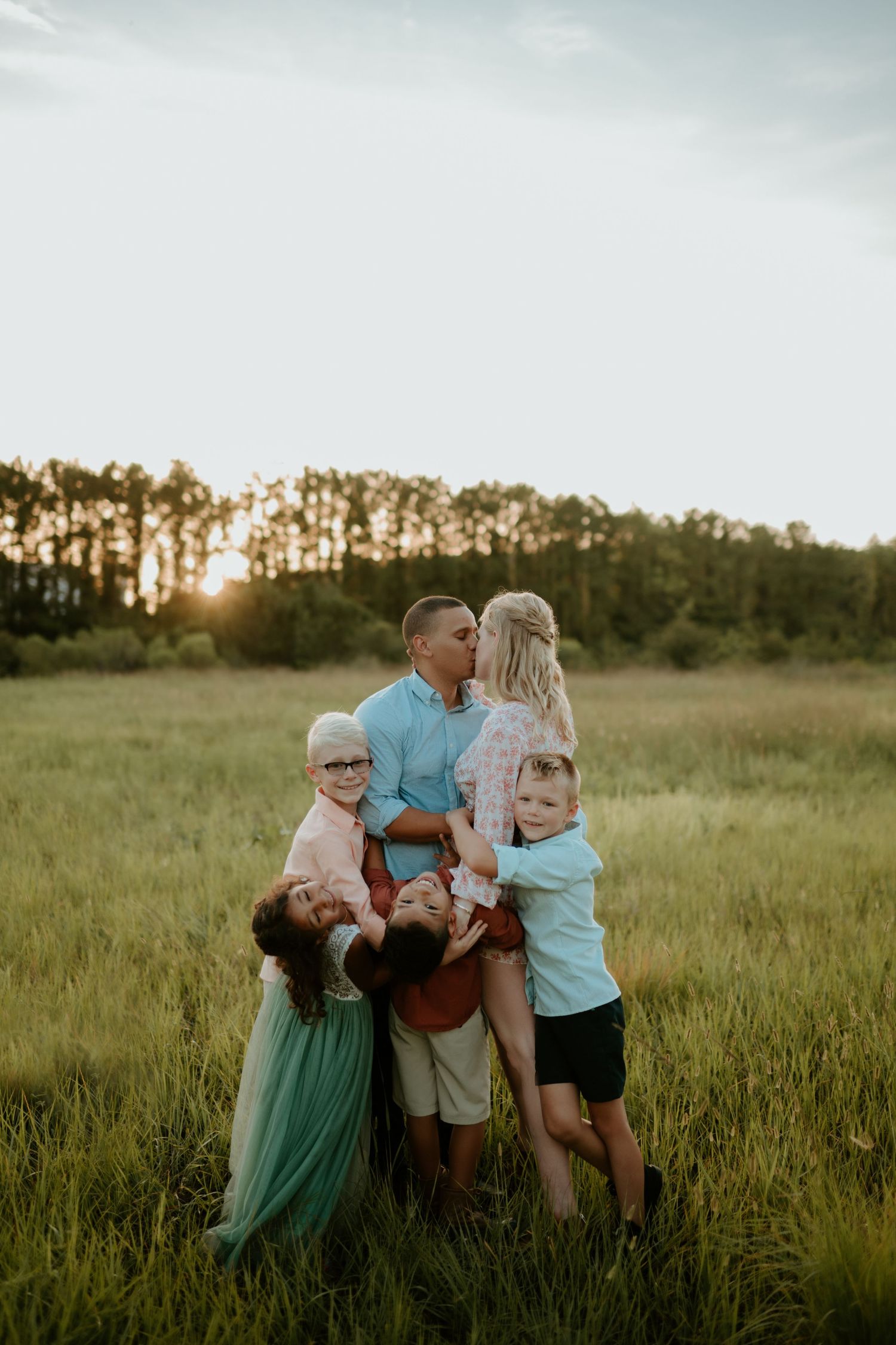 A family embraces while standing together in a grassy field at sunset.