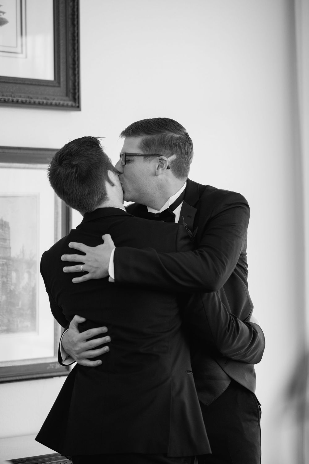 Black and white photo of two grooms sharing a kiss in tuxedos on their wedding day.