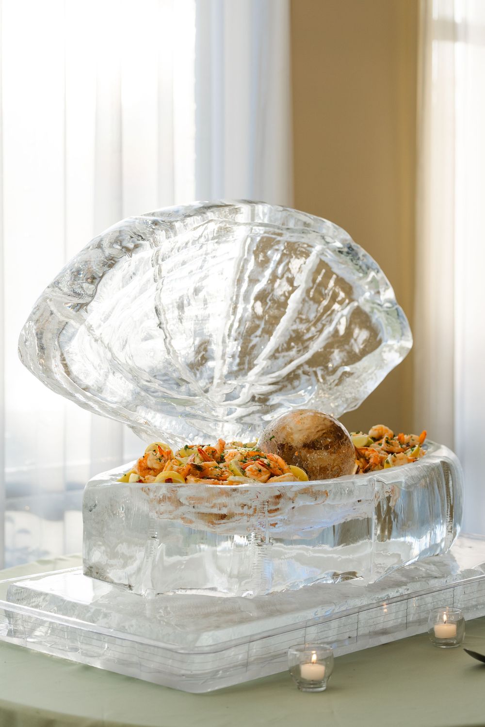 Decorative ice sculpture shaped like an open clam shell filled with shrimp and seafood appetizers.