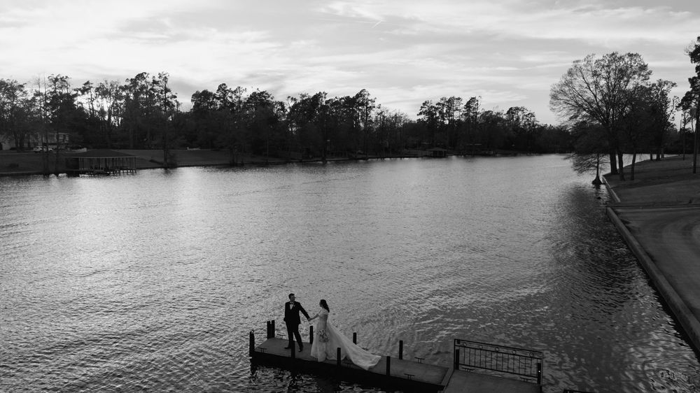 Black and white photo of two people on a dock overlooking a calm river surrounded by trees.