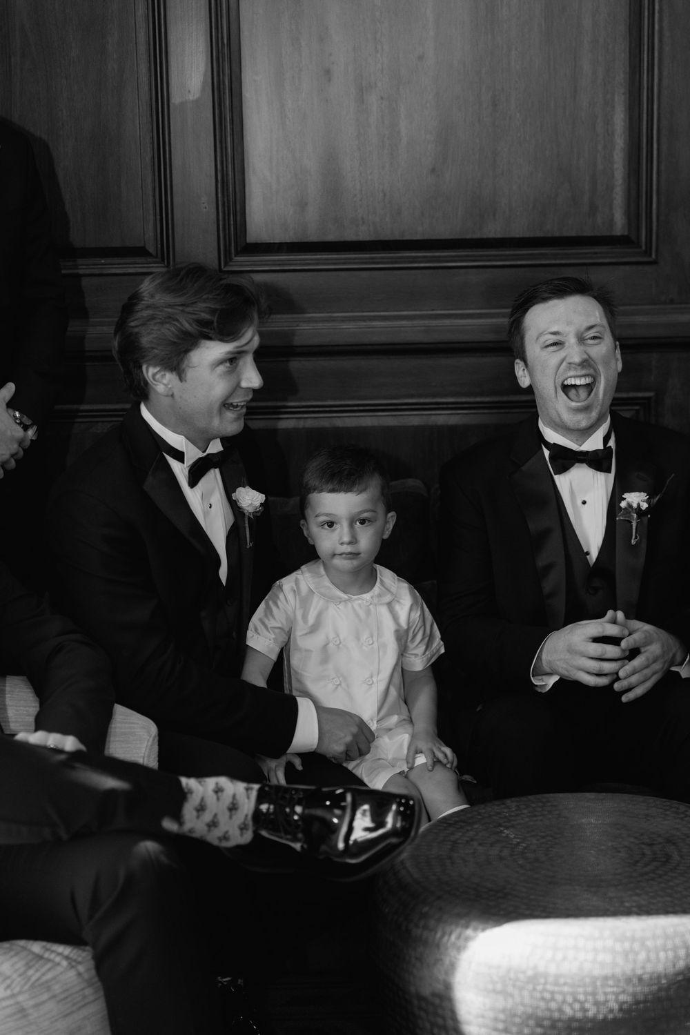 Black and white photo of two men in tuxedos laughing with a young child between them.