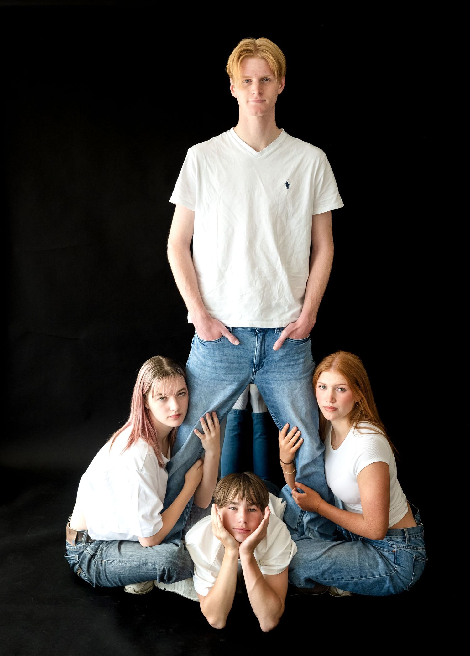 Studio portrait of four people wearing white t-shirts and blue jeans posed in a creative arrangement against black background.