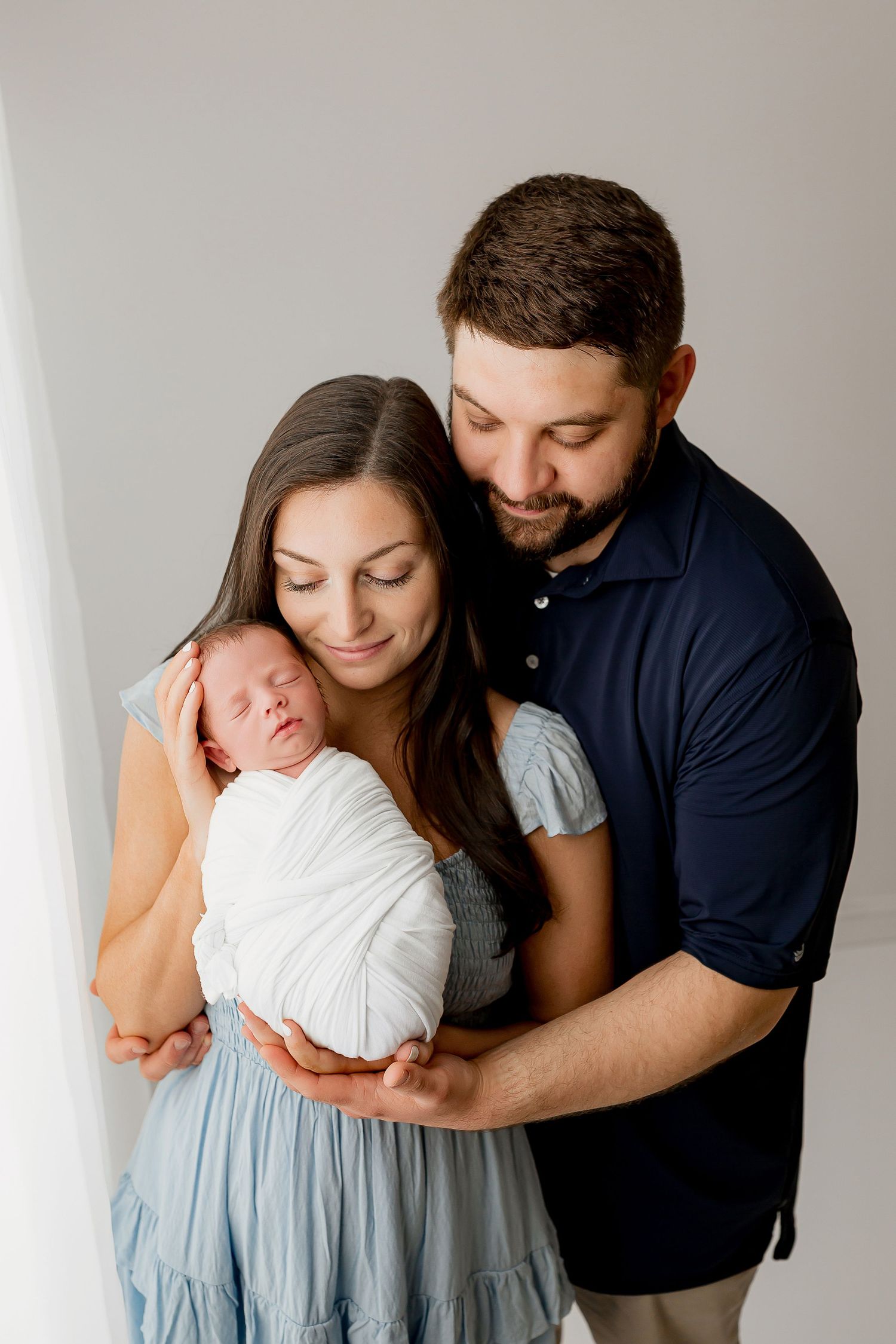 New parents holding newborn baby by window during studio portrait session