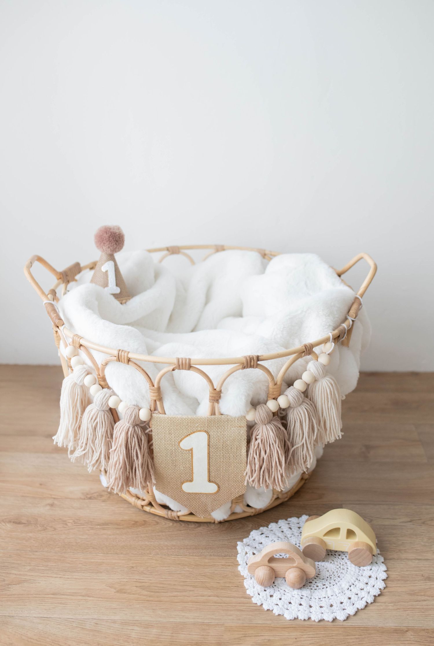 Boho rattan basket with white blanket, number 1 sign, tassels and wooden toys for baby photo prop.