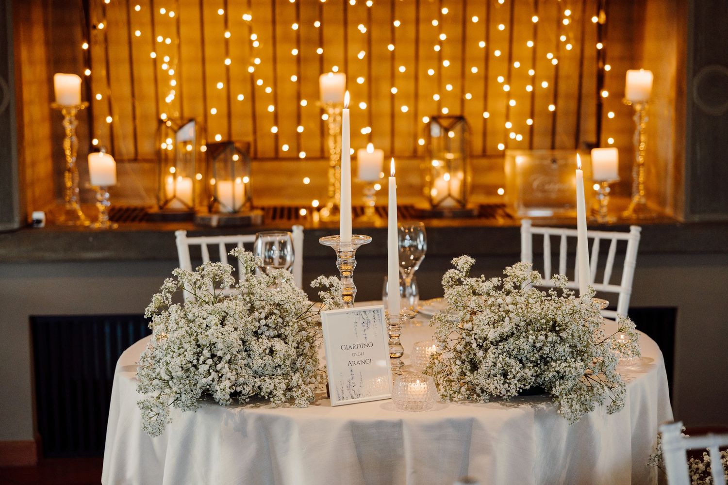 Elegant wedding sweetheart table decorated with white candles, baby's breath flowers, and fairy lights.