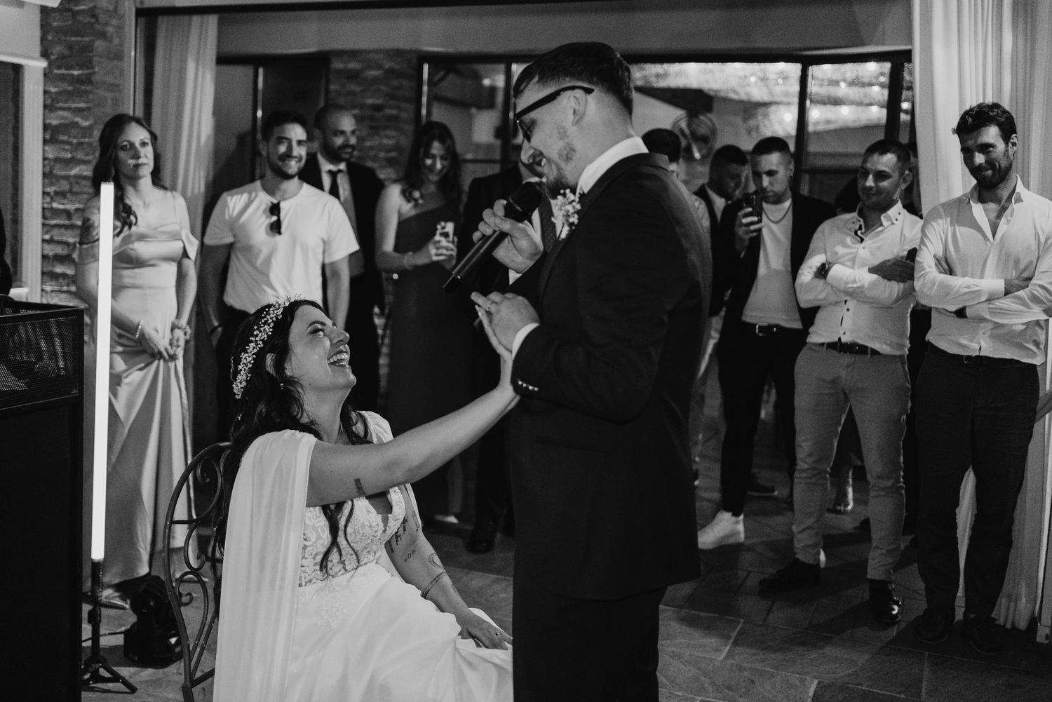Black and white wedding photo of groom holding microphone while bride gazes up at him lovingly.