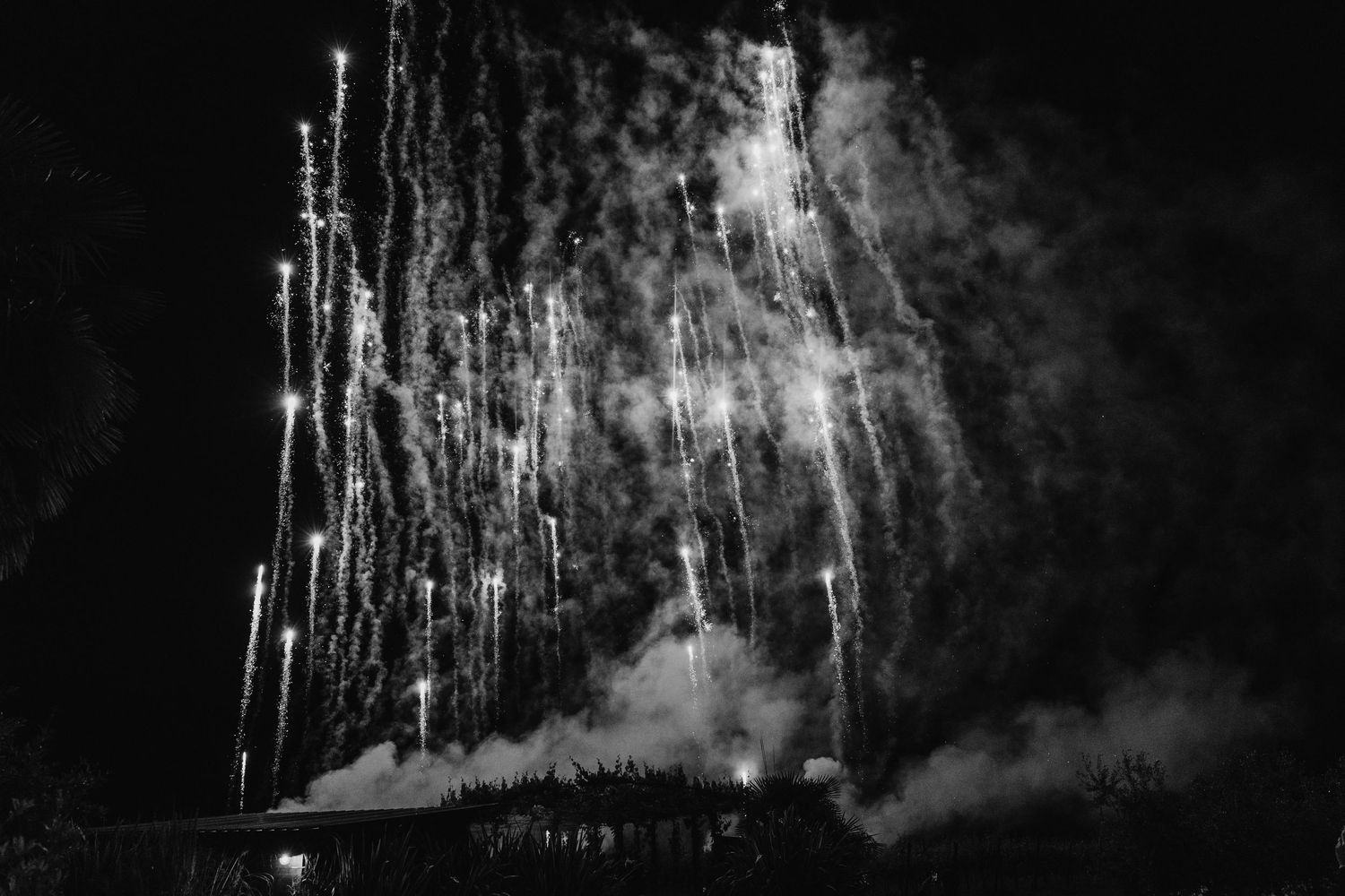 Black and white dramatic fireworks display lighting up the night sky at an outdoor wedding celebration.