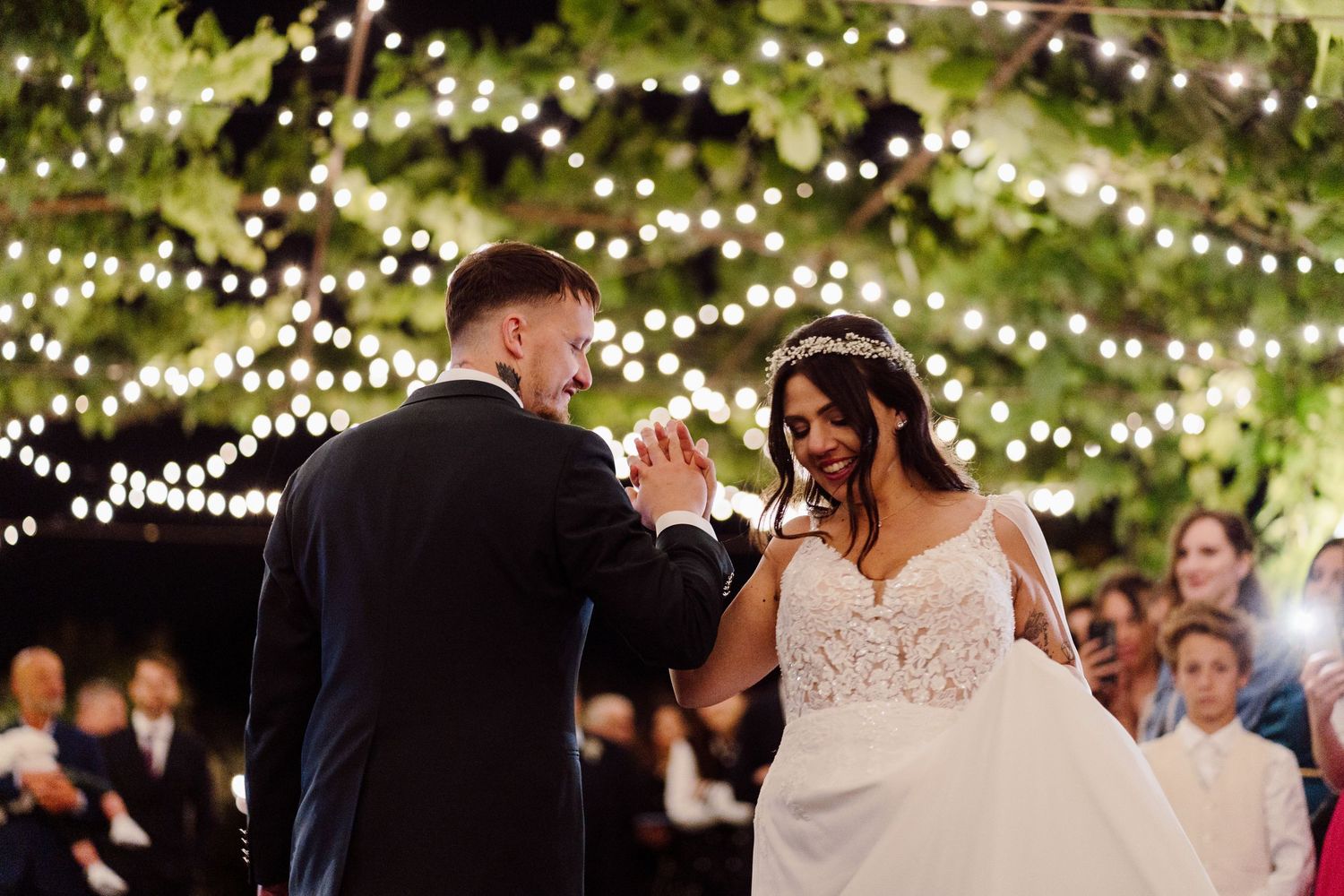 Bride and groom share joyful first dance under twinkling fairy lights at outdoor evening wedding reception.