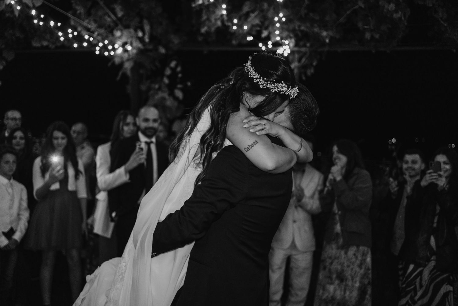 Black and white photo of bride and groom sharing emotional first dance embrace at outdoor wedding reception.