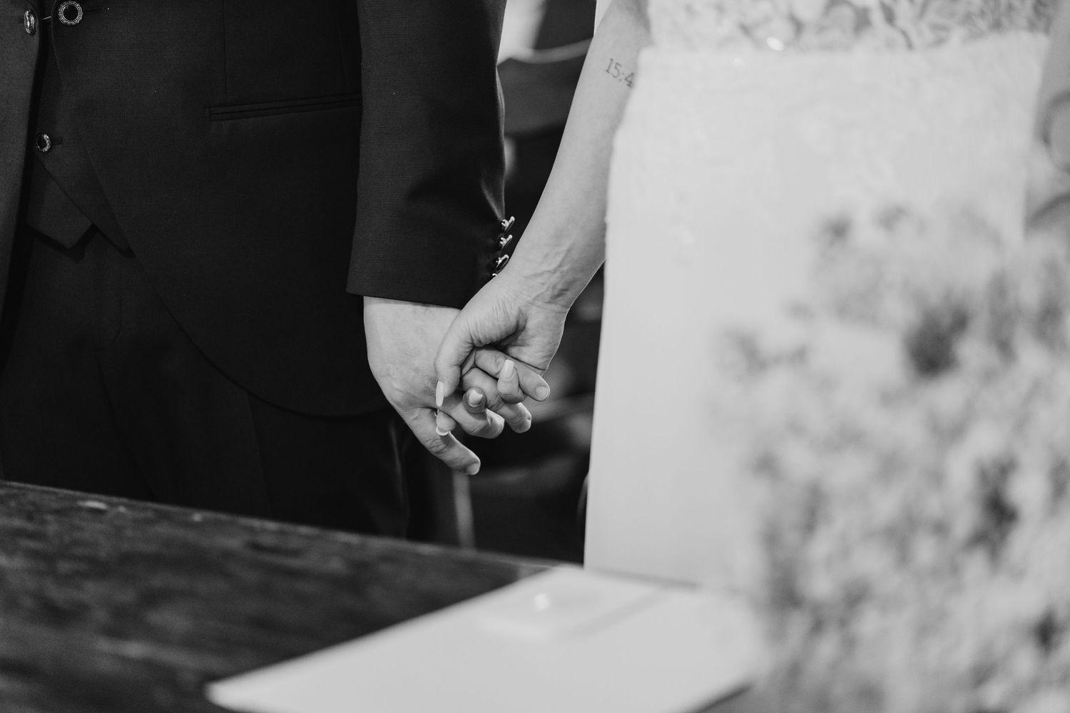 Close-up black and white photo of bride and groom holding hands during wedding ceremony.