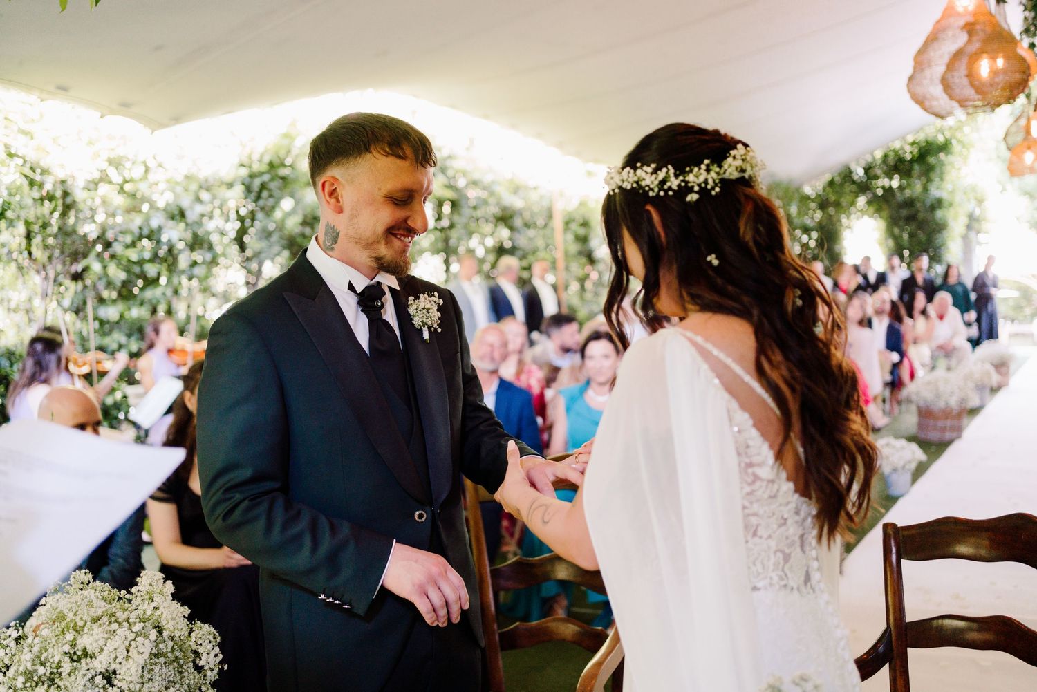 Groom smiles at bride during elegant outdoor wedding ceremony with floral decorations.