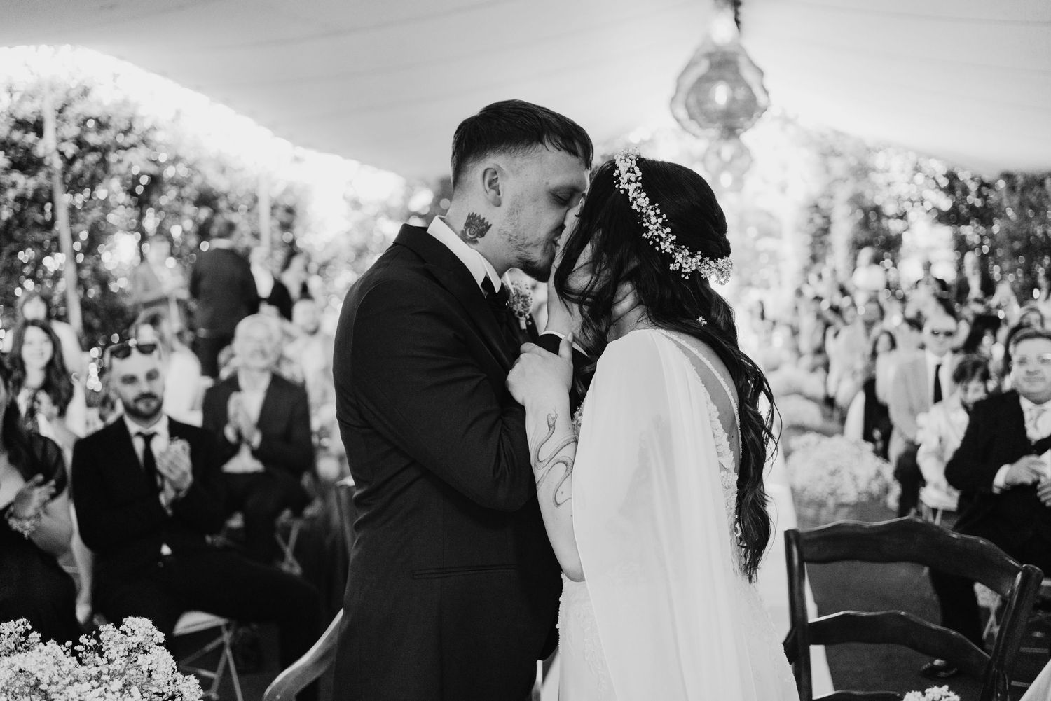 Bride and groom share first kiss at outdoor wedding ceremony in black and white photo.