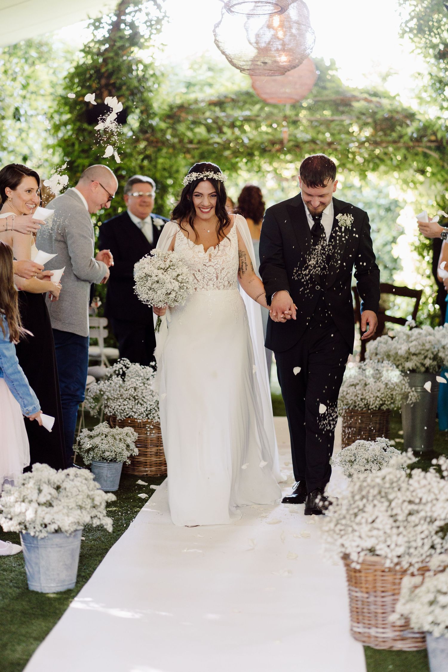 Joyful bride and groom walk down aisle as guests throw confetti at outdoor wedding.