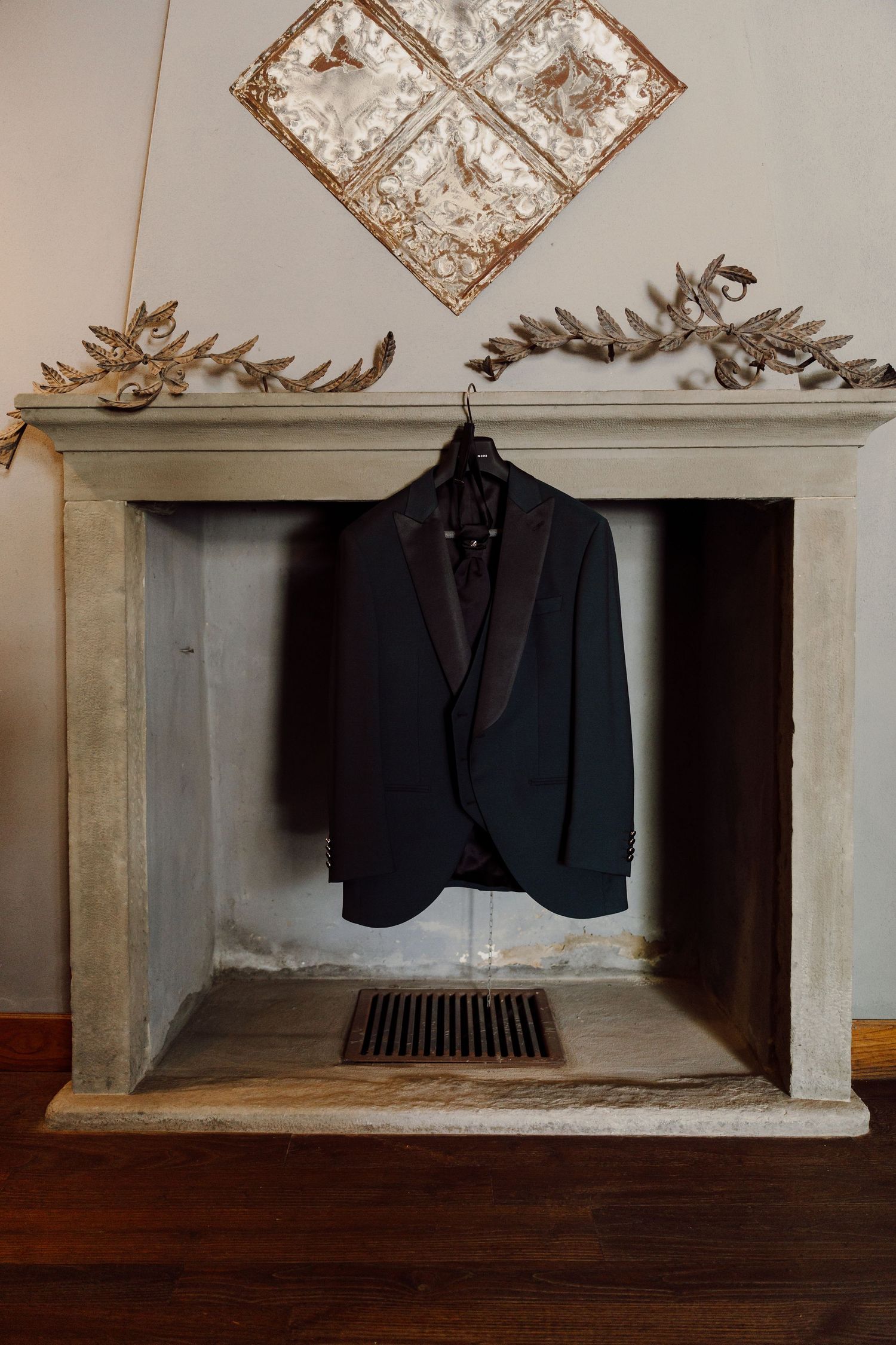 Grooms black tuxedo jacket hanging inside a decorative stone fireplace mantel.