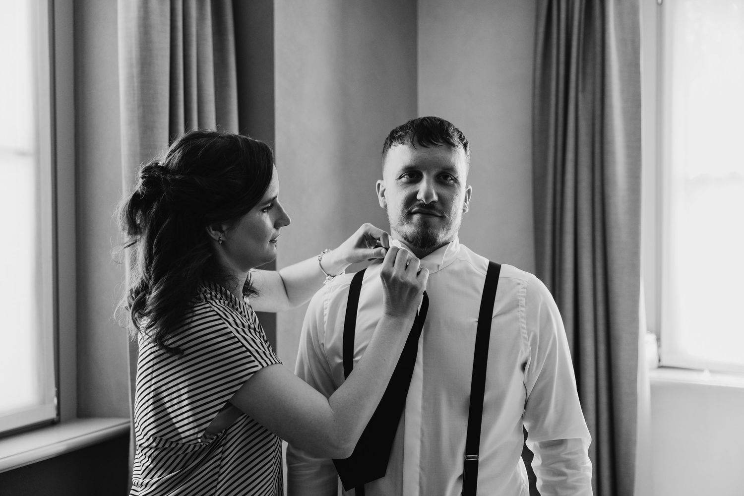 Black and white photo of a woman adjusting the grooms tie before the wedding.