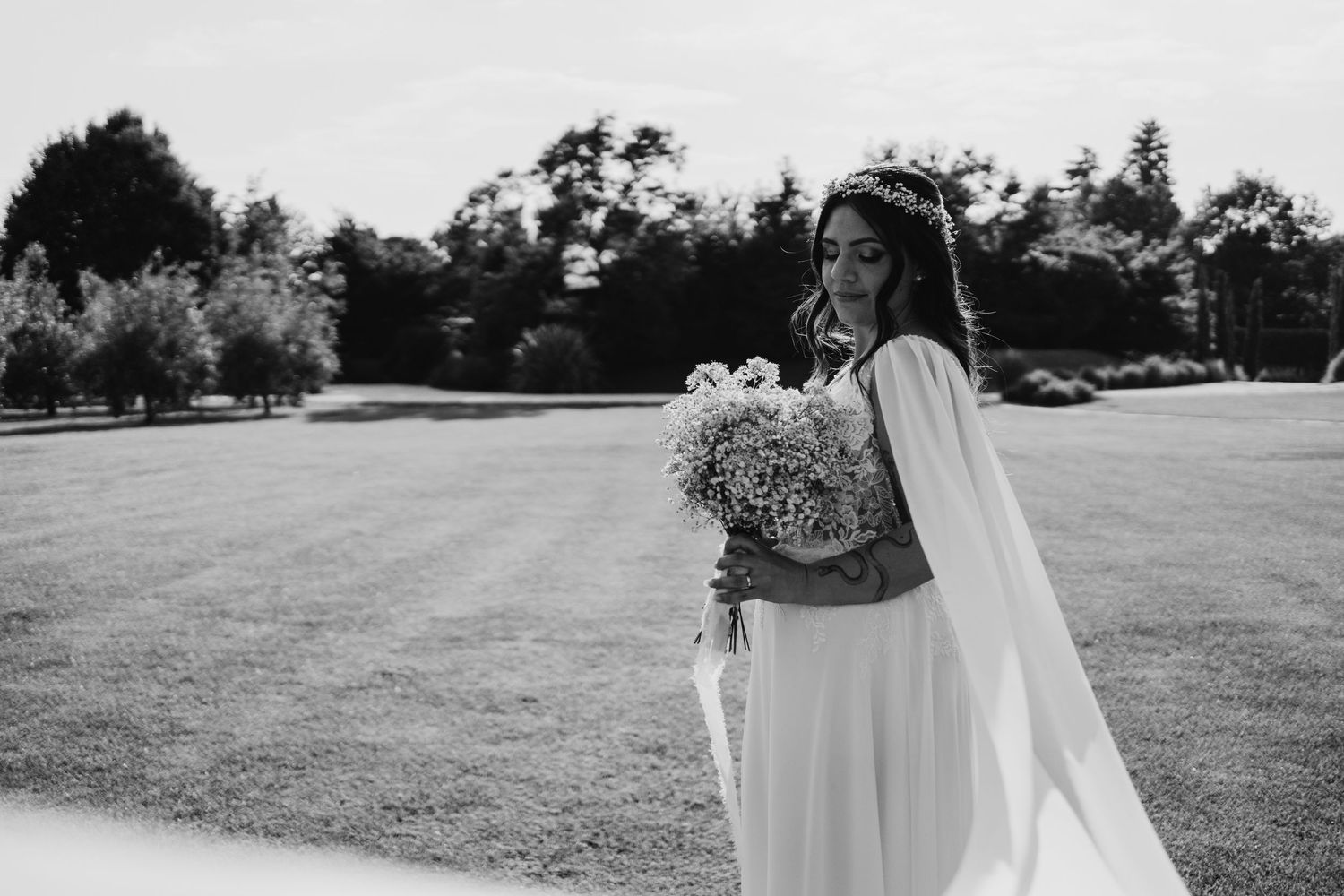 Black and white portrait of an elegant bride holding a baby's breath bouquet on a lush green lawn.