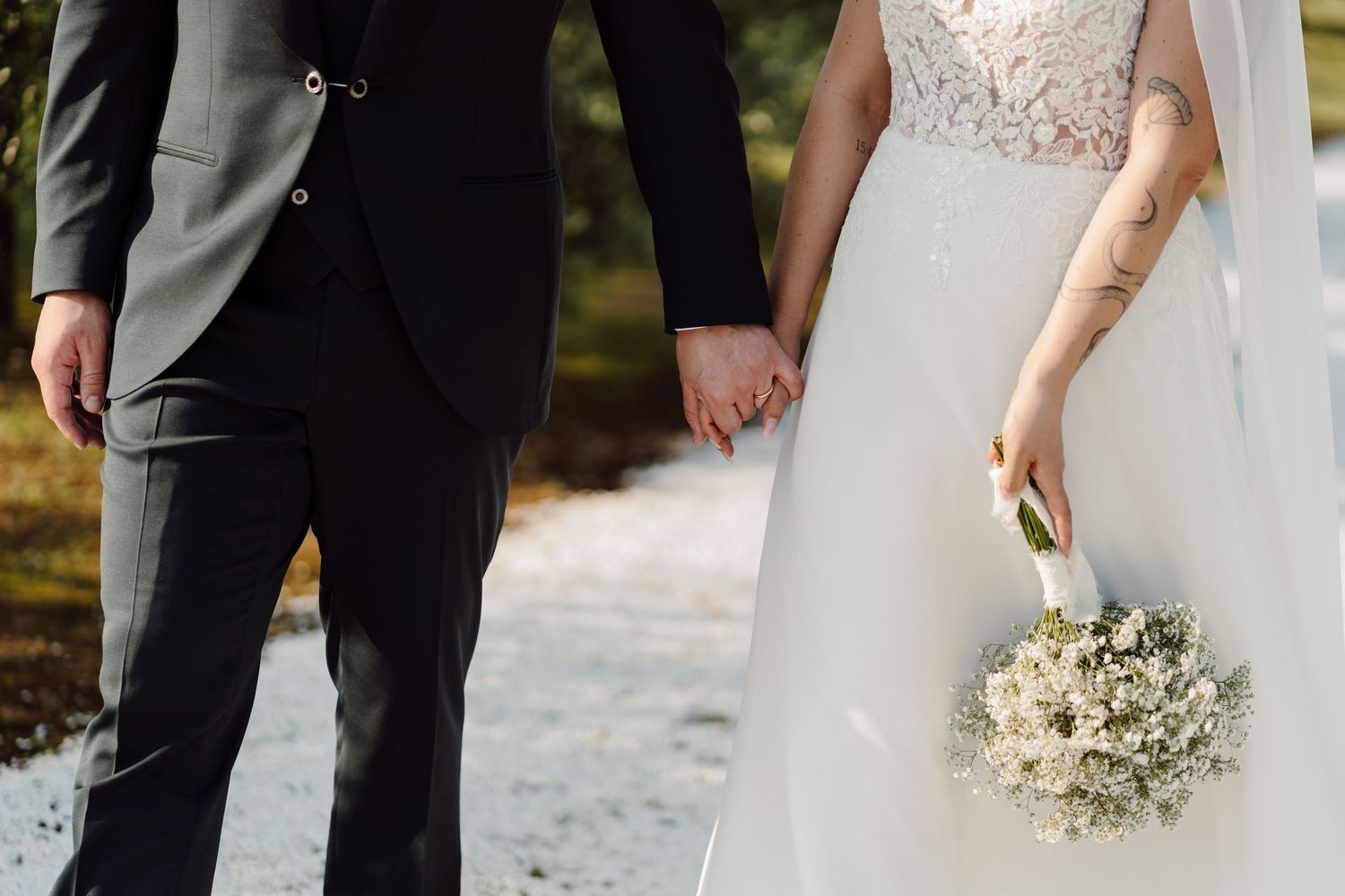 Close-up of bride and groom holding hands, bride carrying a delicate white bouquet on their wedding day.