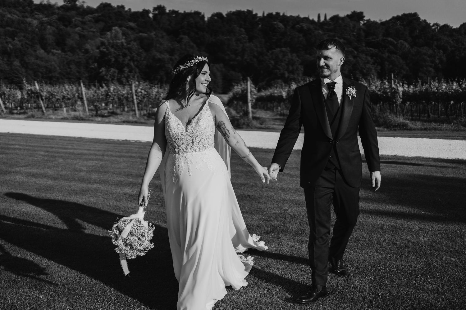 Black and white photo of bride and groom holding hands walking across open lawn.