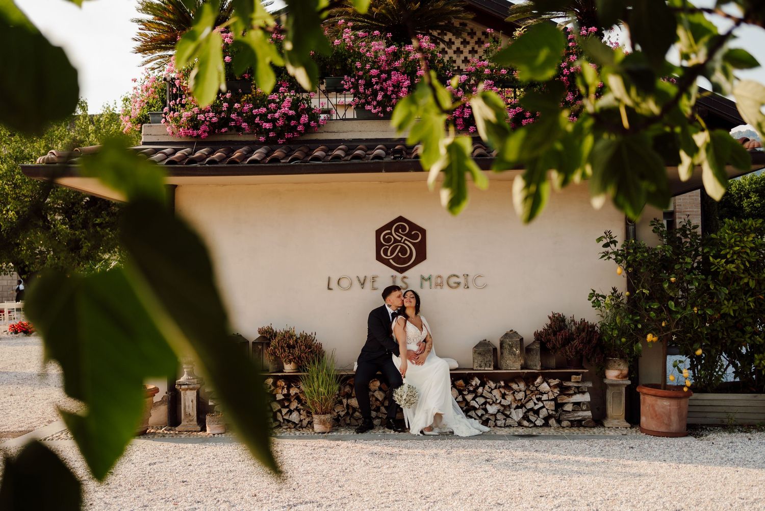 Bride and groom sitting together outside a venue with Love is Magic sign on wall.