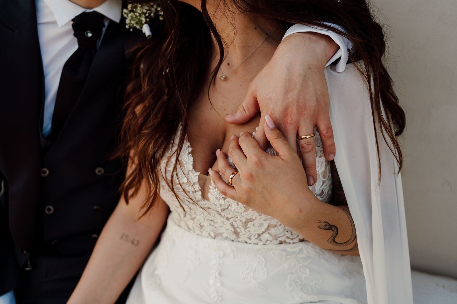 Close-up of bride and groom's hands intertwined showing wedding rings and tattoos.