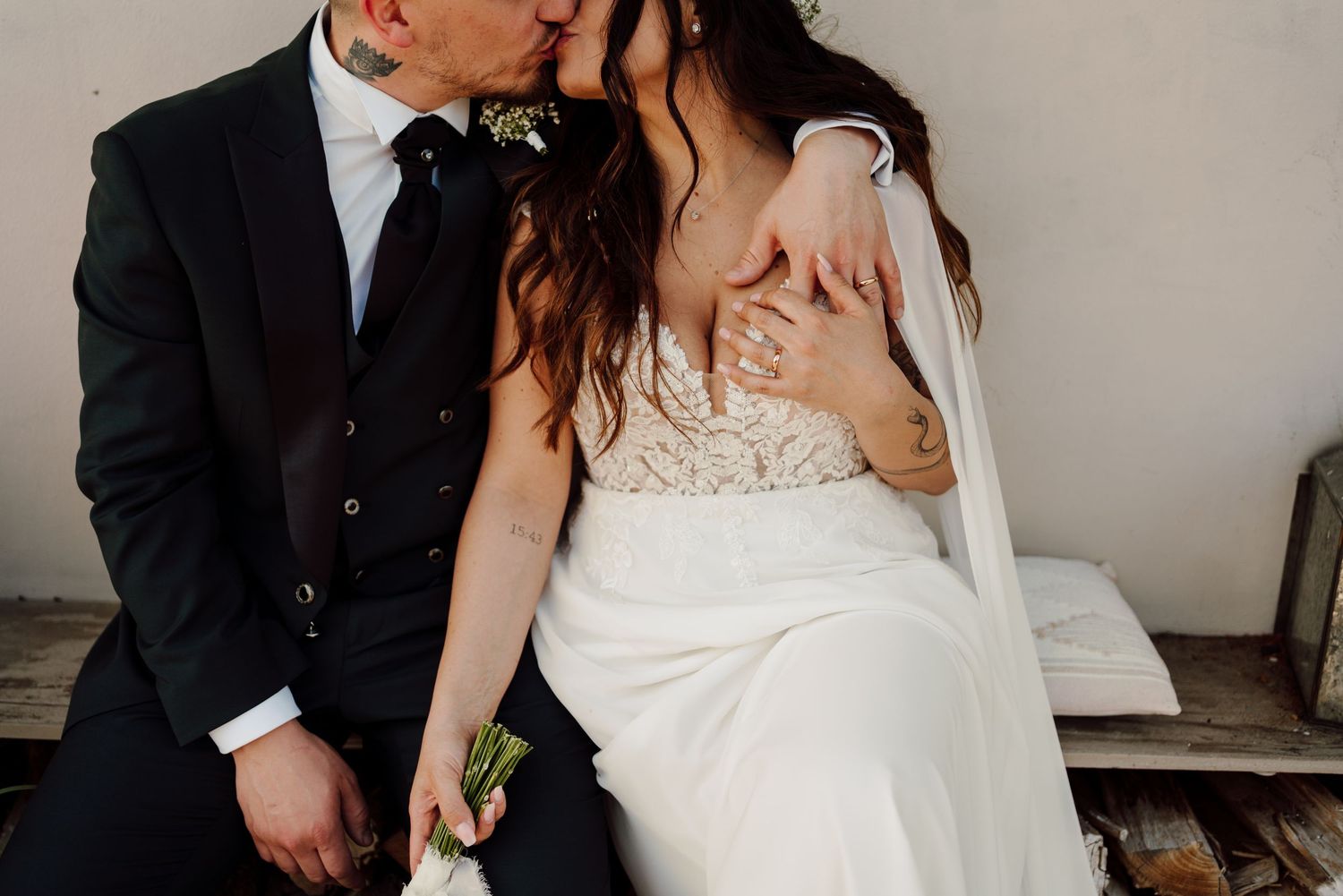 Bride and groom sharing a tender kiss while seated on a bench outdoors.
