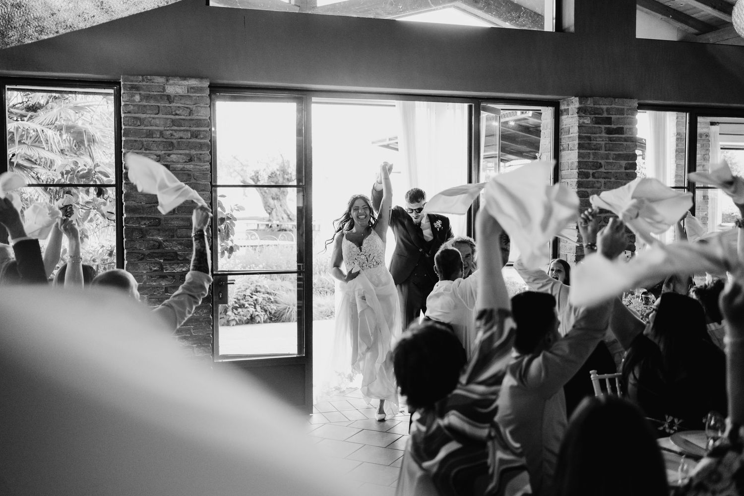 Bride and groom enter wedding reception as guests wave white napkins in joyful celebration.