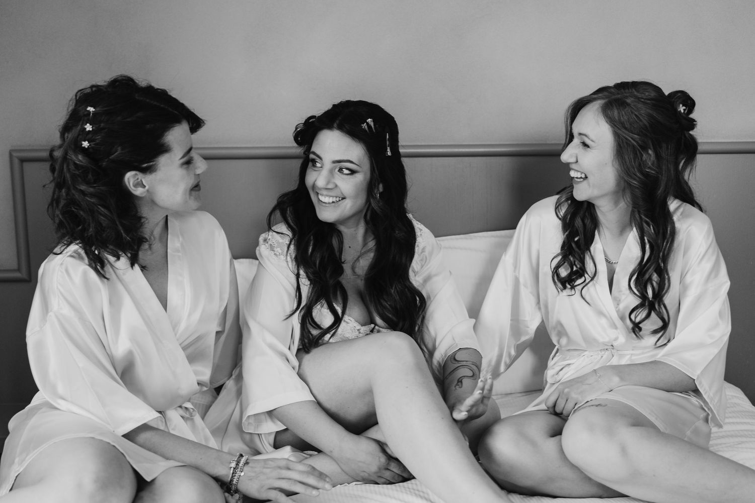 Black and white photo of bride and two bridesmaids laughing together on a bed.