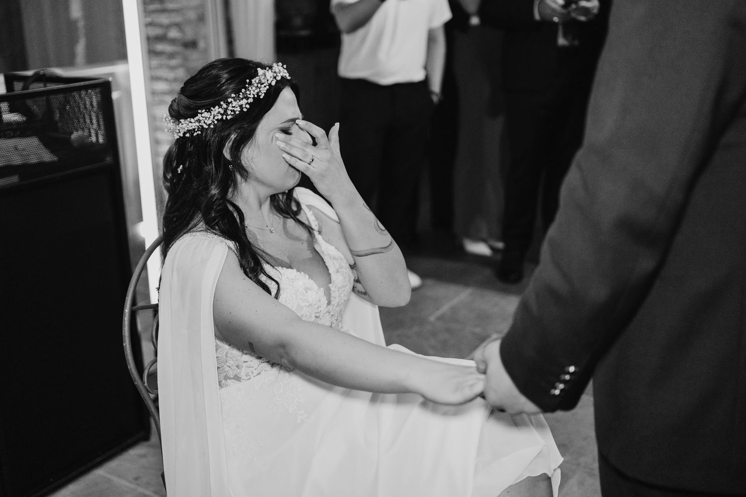 Emotional black and white photo of bride covering her mouth in tears during wedding reception moment.