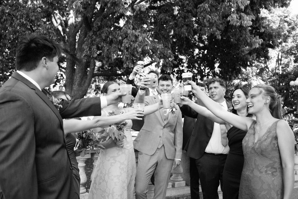 Wedding party celebrates outdoors with joyful expressions and raised arms.
