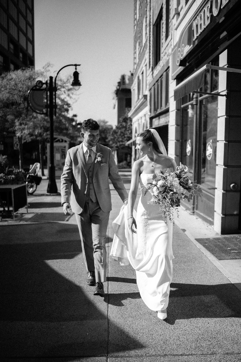 A series of black and white wedding photos showing a couple walking together on a sidewalk in formal attire.