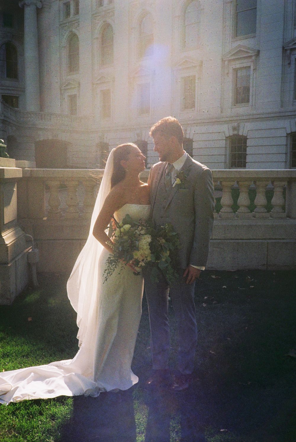 A romantic wedding couple embraces in a series of dreamy sunlit photos outside a grand historic building.