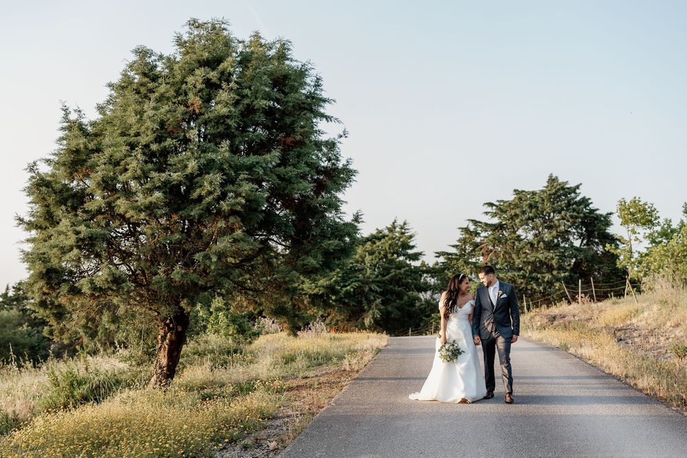 A couple walks hand in hand down a tree-lined country road on a sunny autumn day.