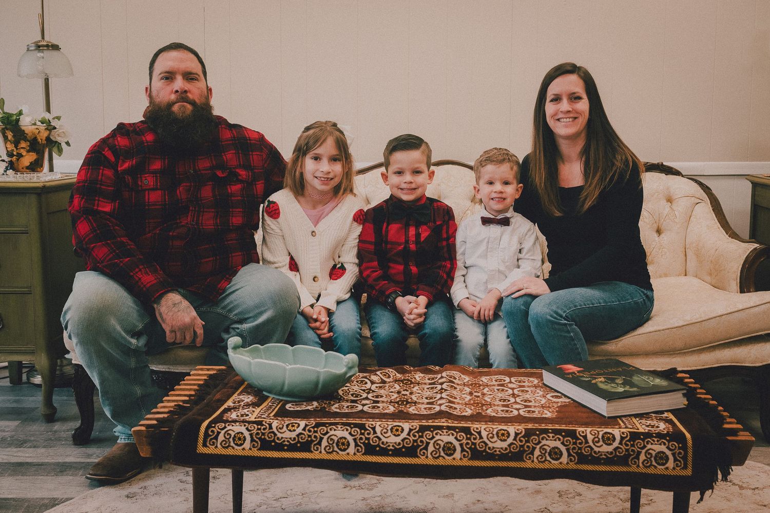 A family sits together on a couch in their living room during a casual indoor photoshoot.