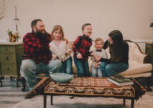 Family sitting together on a brown vintage bench in a casual indoor photoshoot setting.