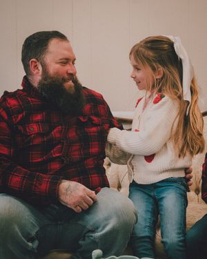 A heartwarming moment between a bearded person in a red plaid flannel and a child in a white sweater sitting together.