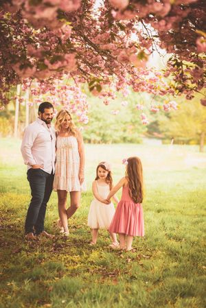 Family enjoying a spring day beneath flowering cherry trees with soft pink petals overhead.