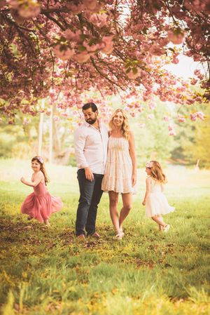 A dreamy spring portrait under blooming cherry blossoms with two children playing in flowy dresses.