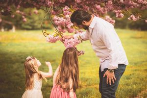 A group of people enjoy a spring day beneath blooming pink cherry blossoms in a sunny garden setting.