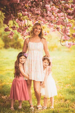A springtime portrait under blooming cherry blossoms with pink and white dresses in a sunlit garden setting.